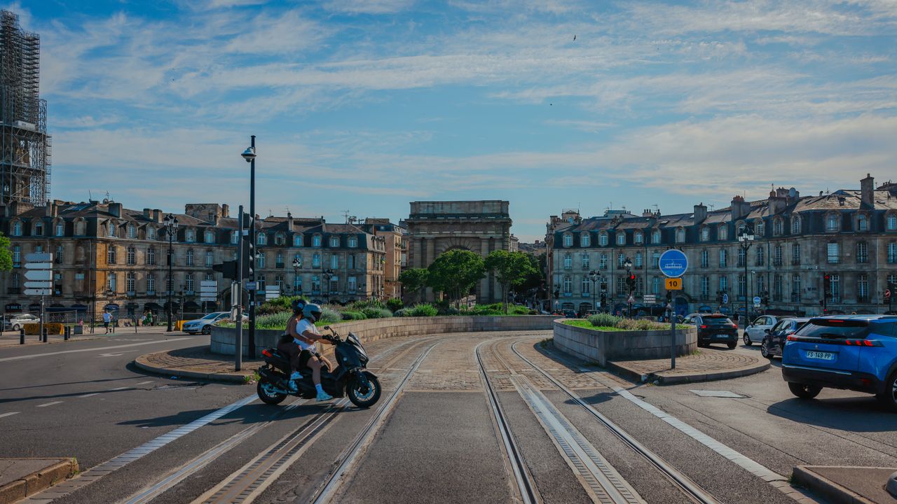 Busy street scene in Bordeaux, France featuring a motorbike and historic architecture on a sunny day.